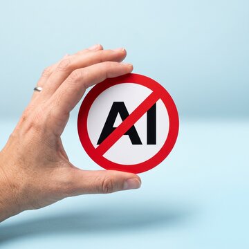 Hand holding no artificial intelligence prohibition sign against AI background