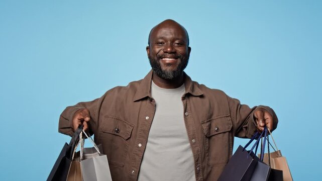 Portrait of African American man holding shopping bags and smiling at camera in studio. Clip ideal for retail advertising, holiday sales promotions and consumer marketing