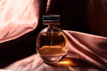Bottle of aromatic perfume on brown silk, closeup