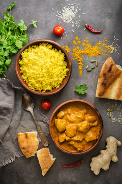 Chicken tikka masala in a bowl with basmati rice and naan bread on a dark rustic background, top view, flat lay. Traditional spicy Indian dish.