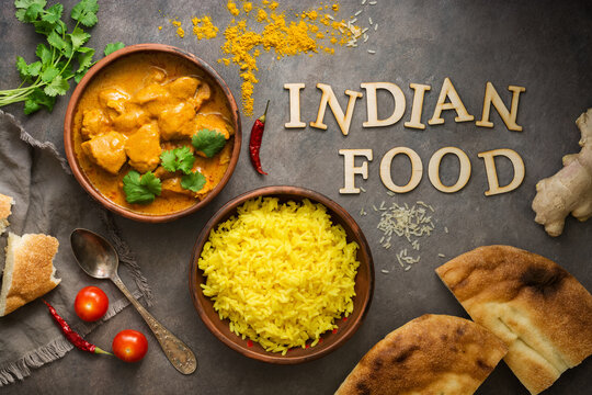 Chicken tikka masala in a bowl with basmati rice and naan bread on a dark rustic background, top view, flat lay. Traditional spicy Indian dish.