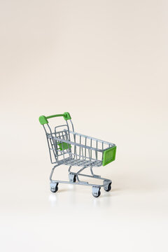 Empty miniature shopping cart with green handle on light background with copy space