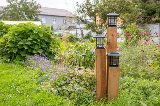 Decorative wooden posts with outdoor lanterns in a green flower garden in daylight