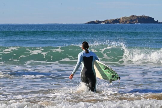 A surfer carries a surfboard and enters the ocean for a session off the coast of Ferrol, Galicia, Spain. A coastal landscape featuring the Atlantic Ocean,August 30, 2026