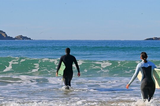 A surfer carries a surfboard and enters the ocean for a session off the coast of Ferrol, Galicia, Spain. A coastal landscape featuring the Atlantic Ocean,August 30, 2026
