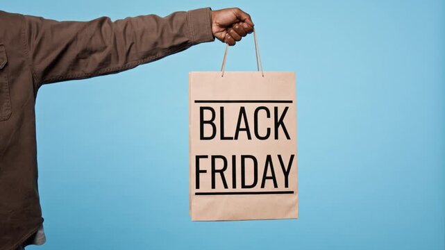 Unknown man holding paper shopping bag with Black Friday text against blue background. Ideal for holiday retail promotions, seasonal sales campaigns, and commercial ecommerce advertising