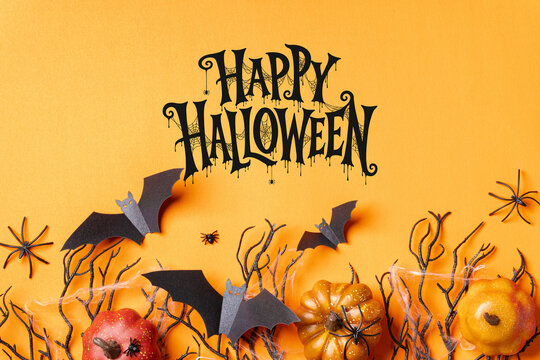Happy Halloween lettering with pumpkins, flying bats, spiders and twisted branches on a warm orange background, ideal for cards, invitations, posters and seasonal advertising.