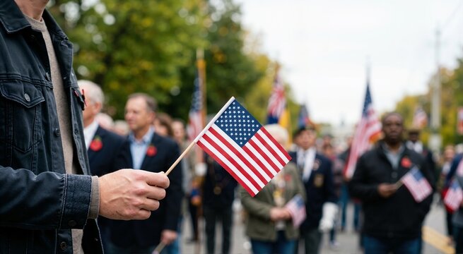 Close up of a man holding a small American flag. Veterans Day or Memorial Day tribute parade concept. Blurred crowd background