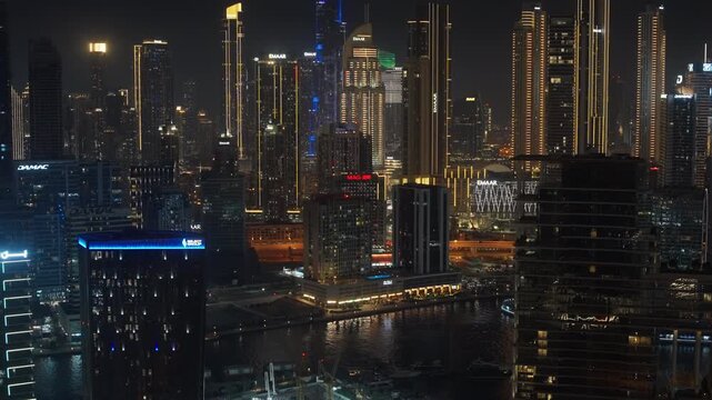 DUBAI, UAE - AUGUST 29, 2026: Emaar and DAMAC signs on real estate towers glow above the waterway in Dubai UAE, as traffic passes at night