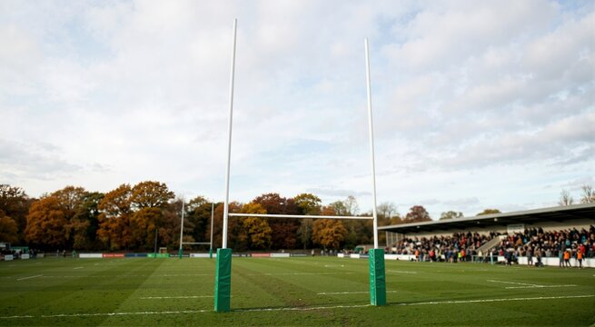 Rugby goal posts on a green grass field. Stadium stand with spectators and autumn trees under cloudy sky
