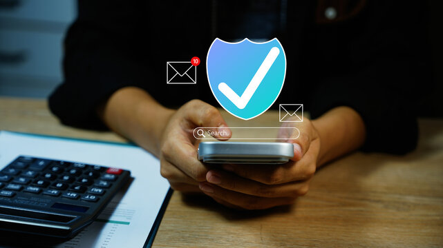 Holographic mobile security and email verification, Person using a smartphone with a digital security shield, check mark and email alerts beside a calculator and financial papers.