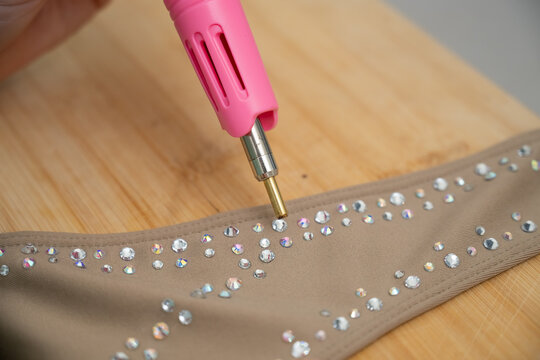A woman glues rhinestones onto a gymnastics costume using a soldering iron. Hot fix.
