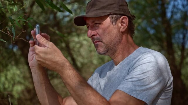 Man using a smartphone to capture nature photos and video along a scenic riverbank. Concept of mobile photography, outdoor content creation, digital travel vlogging, and modern leisure. 4K.