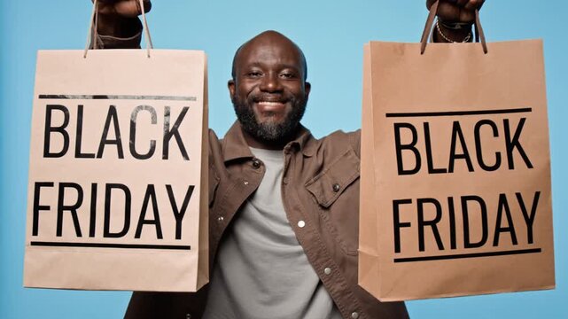 Portrait of smiling African American man showing paper shopping bags with Black Friday text. Footage suited for seasonal sales promotion, commercial retail campaigns and discount ads