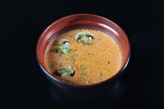 Spicy creamy mushroom soup in dark ceramic bowl. Sliced mushrooms and scallions garnish. Gourmet appetizer. Black background highlights color