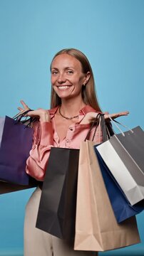 Portrait of cheerful Caucasian young adult woman lifting shopping bags while looking at camera. Footage suitable for retail advertising, seasonal sale promo, e-commerce marketing, vertical