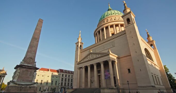 At Alter Markt in Potsdam, Germany, St. Nicholas Church and its neoclassical dome rise beside the Potsdam Obelisk at golden hour.