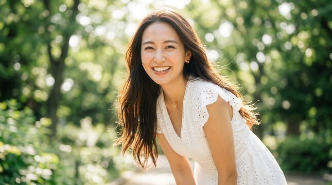 Smiling adult woman in a white dress leaning forward within a green park setting