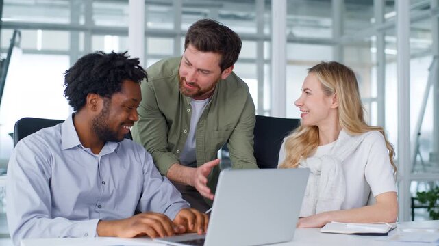 Three diversity excited business partners team smiling looking in laptop computer winning celebrating successful work businesswoman dancing happy Caucasian boss talking African businessmen in office