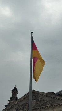 Flag of Germany waving in the wind with a background of german Reichstag building and grey moody sky. Political symbol of european country
