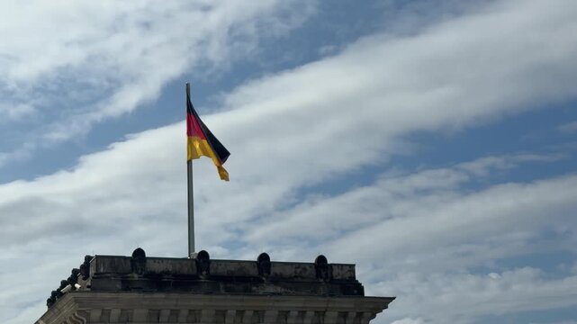 German flag on Bundestag top under blue sky with puffy clouds. Main symbol of Germany on parliament building in Berlin close up
