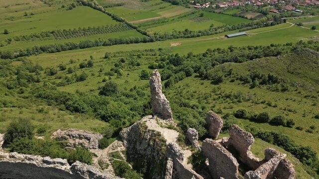 Medieval fortress ruins standing on a rocky mountain slope with green hills and blue sky