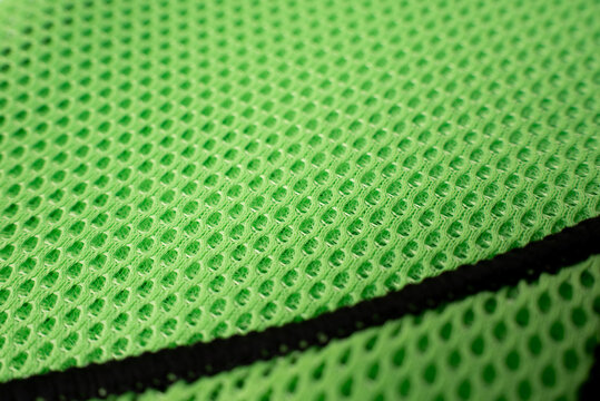 Macro shot of bright green mesh fabric with black piping edge. Texture of breathable neon green polyester material used for sportswear, safety vests, or industrial apparel.