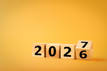 Obraz premium New Year 2027. Wooden cube flipping changing number from six to seven against orange background
