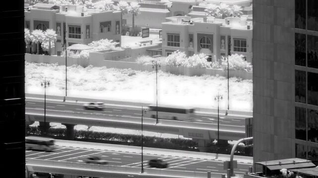 Infrared timelapse of traffic moving along a multi lane city highway, with residential buildings and white palm trees visible under bright daylight