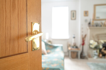 Obraz premium Shallow focus of a gold coloured door hand leading to a large living room. A sofa together with a fireplace can be seen.
