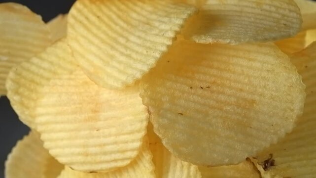Ridged potato chips falling in slow motion on black background