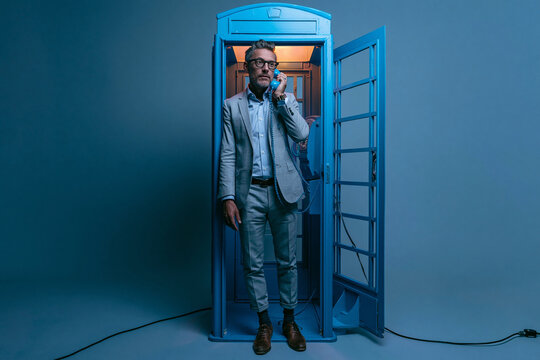 Businessman in Suit Talking on Phone in Blue Booth