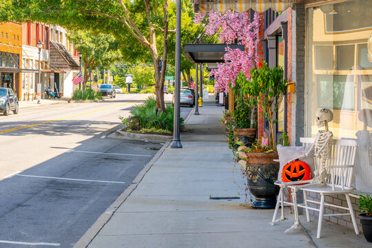 The tree lined Main Street decorated for the fall season with a life size skeleton on a storefront bench holding a pumpkin in the small town of Lake City, South Carolina.
