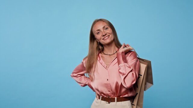 Portrait of young adult Caucasian woman holding Black Friday shopping bags over shoulder on blue studio background. Visual serves retail sales promotions and holiday marketing campaigns