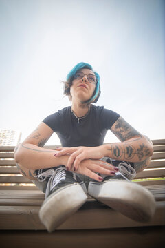 Pensive gen z alternative woman with blue hair sitting on bench with copy space