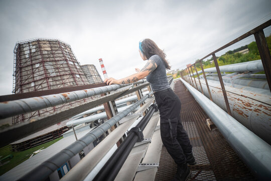 Alternative gen z woman exploring industrial power plant infrastructure with copy space