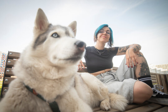 Happy gen z alternative woman with blue hair relaxing on bench with husky dog and copy space