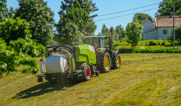 Lindesnes, Norway - June 15 2026: Tractor and baler moving across rural hay meadow.