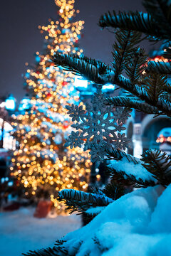 Snow Covered Christmas Tree Branch With Glittering Lights and Snowflake Ornament in Festive Street