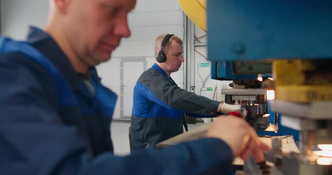 Metal component manufacturing line with workers operating stamping equipment in a factory environment