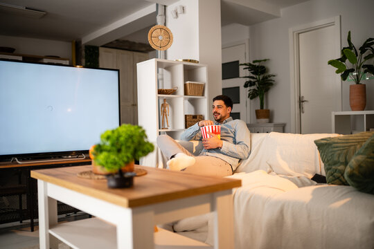Man relaxing at home watching tv and eating popcorn