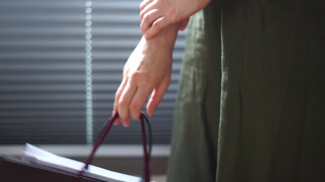 Black Friday shopping consumption Close up of hand gripping red shopping bag strap beside dark green sleeve in softly blurred indoor room with blue blinds and subdued light calm casual commerce mood