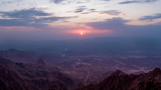 Scenic aerial view of golden morning sun rising through purple dawn skies over rugged mountain peaks and vast valleys in Neom
