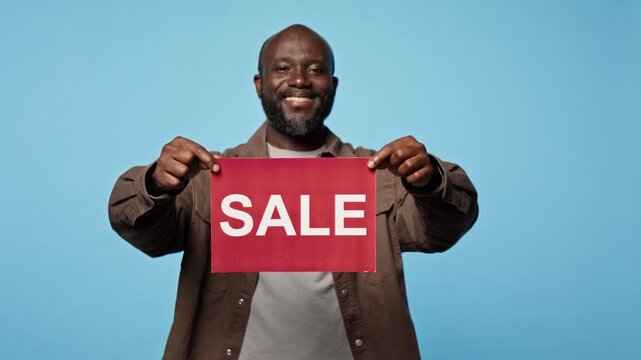 Portrait of joyful African American man holding red sale sign while smiling at camera. Perfect for e-commerce marketing, seasonal sales campaigns, and retail discount advertising