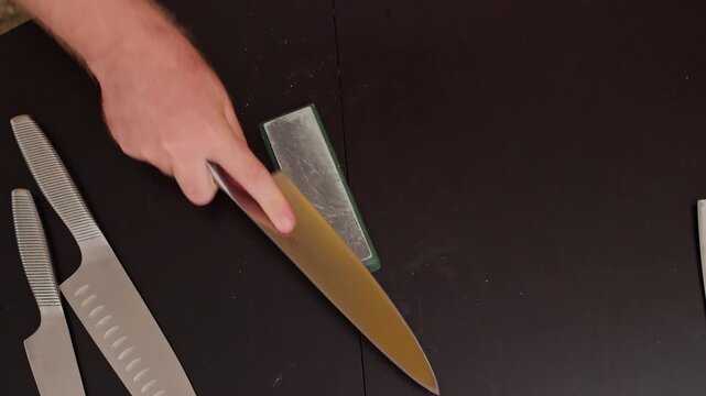 Close-up of hands sharpening kitchen knife on whetstone. Routine knife care in home kitchen