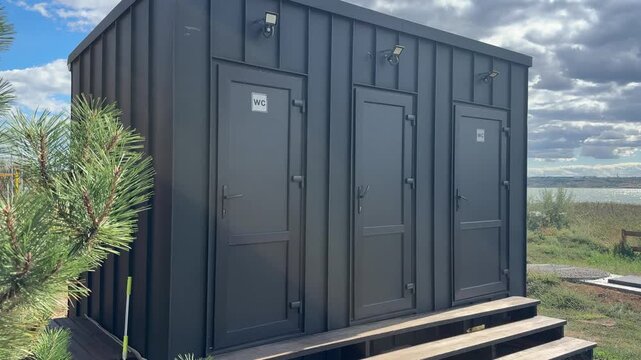 Modern outdoor restroom facility with three stalls and wooden steps