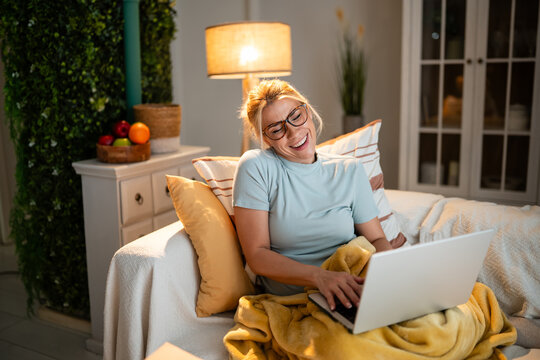 Woman laughing on sofa with laptop cozy at home