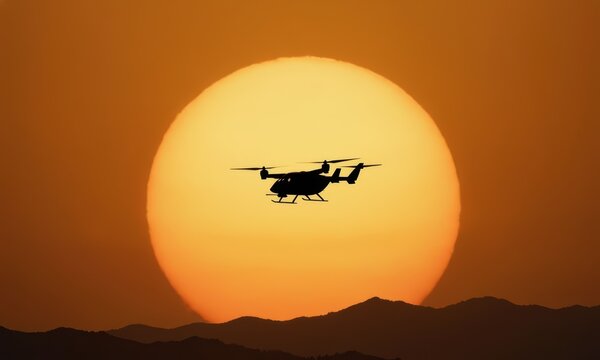 A vtol air taxi hovers against a large sun, casting a silhouette. This vtol air taxi is poised above mountains, reflecting a modern approach to urban transport.