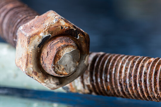 Close up view of a thick steel bolt and nut covered with aged paint and natural rust, rough metal texture, corrosion structural steel components