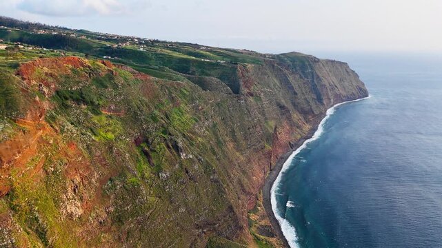 Madeira coastal escarpment stretching toward distant Atlantic headland, Portugal. High sea cliffs below island settlements and rolling uplands